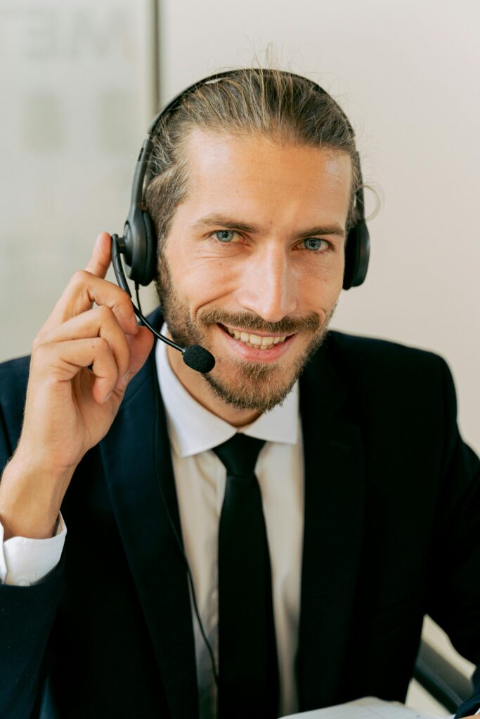 Smiling customer service agent with headset offering assistance in office setting.